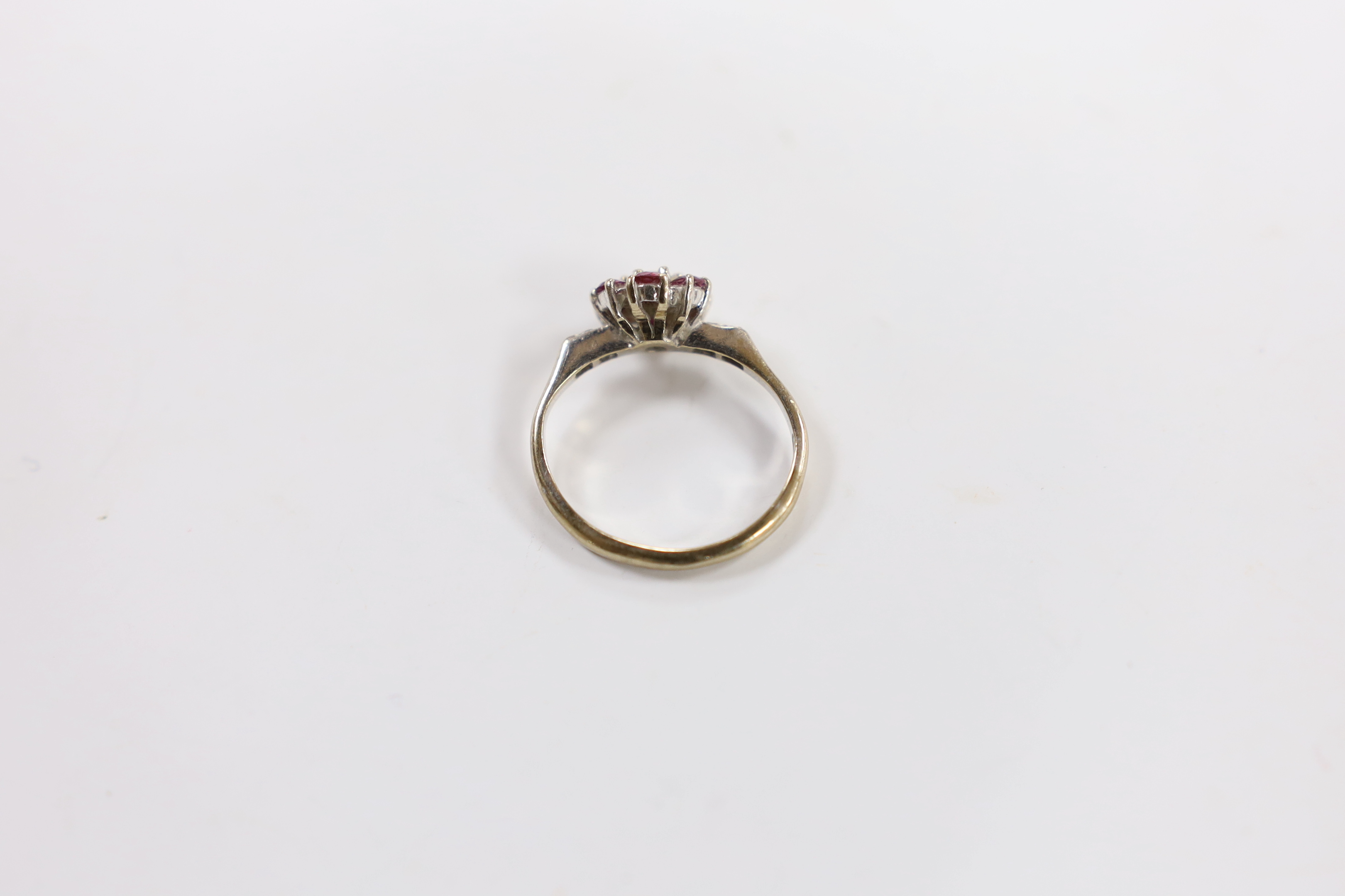 An 18ct white metal, ruby and diamond cluster set flower head ring, with diamond chip set shoulders, size I, gross weight 3.1 grams.
